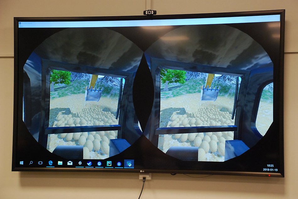 En skärm som visar det som syns i VR-glasögonen: hur man sitter i en grävskopa och ser skopan och diverse sten som ska flyttas. 