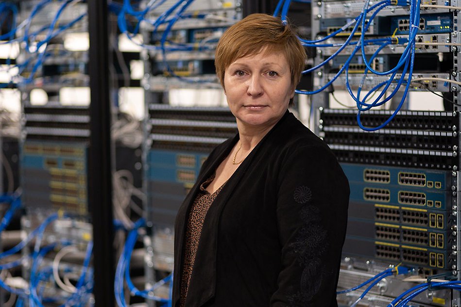  A woman stands by a large number of computer servers and looks into the camera.
