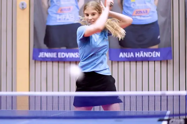 En blond tjej slår en pingisboll över nätet. Foto.