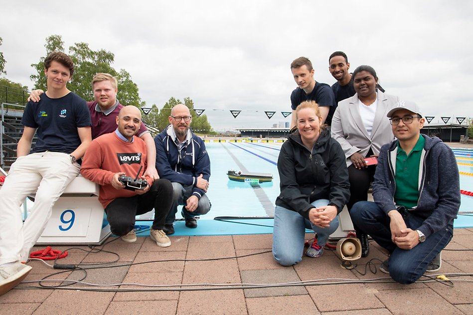 A group photo of nine people with the prototype in the pool in the background.