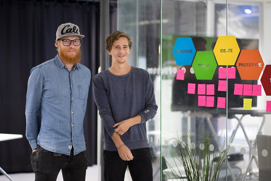 Två killar står vid en glasvägg med post it-lappar och textplattor.