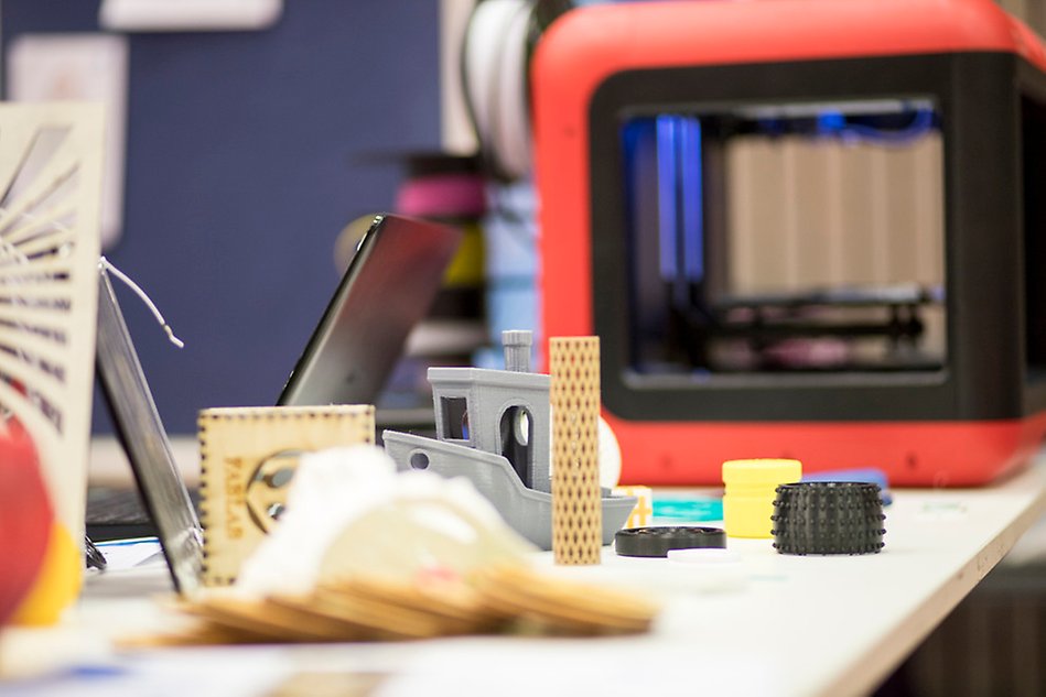 Close-up of a 3D printer with several printed small things in the foreground. Photo.