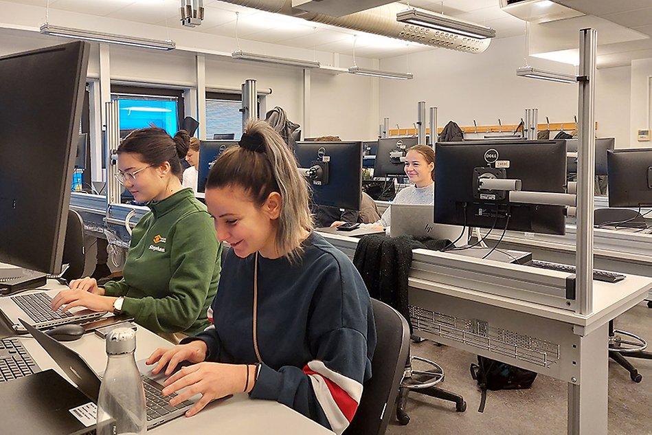 Students sitting in a computer lab and solving digital challenges on each computer. Photo.