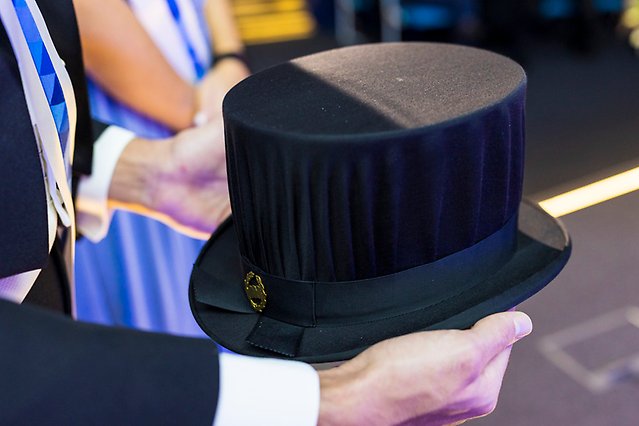 Två händer håller i en hög svart hatt. Foto