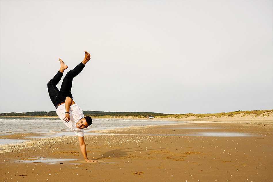 A young man doing a handstand on the beach. Photo.