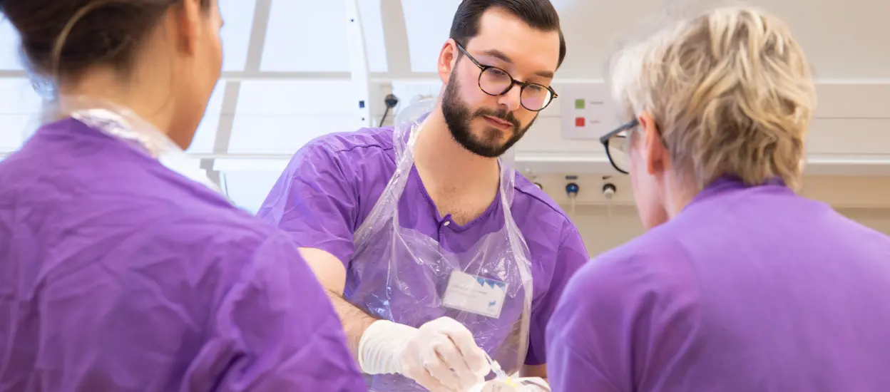 En manlig sjuksköterska tar en slang från en lärare som står med ryggen mot kameran. Foto.