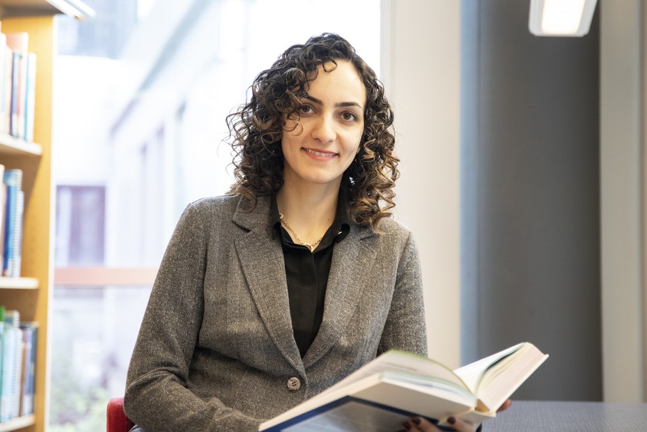 A smiling woman with curly dark hair holding an open book. Photo.