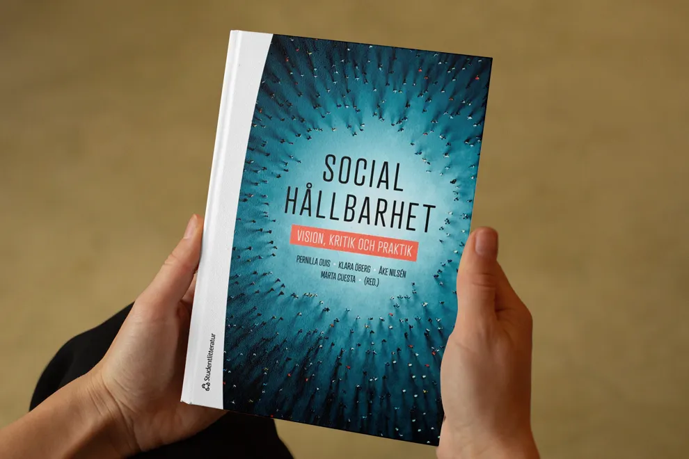 Två händer håller i en bok. Foto.