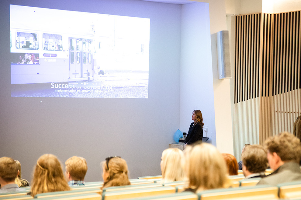 En kvinna står i en stor föreläsningssal och håller en presentation inför publik.