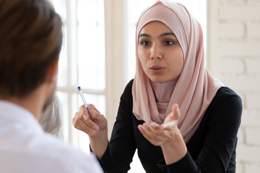 En kvinna klädd i hijab pratar med en annan person i ett möte. Foto