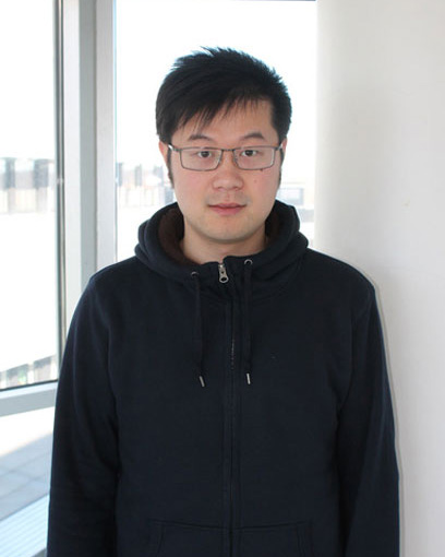 Man with glasses, dark hair and a dark blue top. Bright back ground.