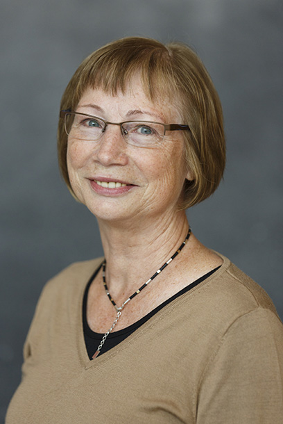 A person with light hair and glasses smiles into the camera. Portrait photo.