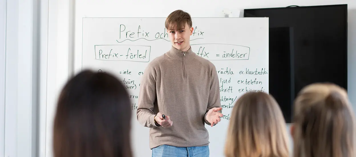 En lärarstudent står vid en whiteboard och pratar inför några personer