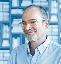 Man with short gray hair and beard and light button up looking into the camera.