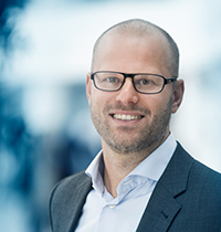 Man with glasses and suit jacket looking into the camera smiling.