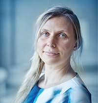 Woman with long blond hair in ponytail looking into the camera at an angle.