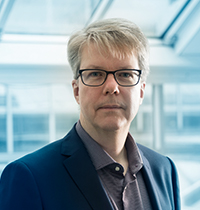 Man with grey hair and black glasses looking into the camera.
