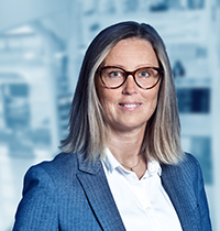 Woman with glasses, suit jacket and long hair looking into the camera.