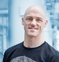 Bald man with black t-shirt looking into the camera smiling.