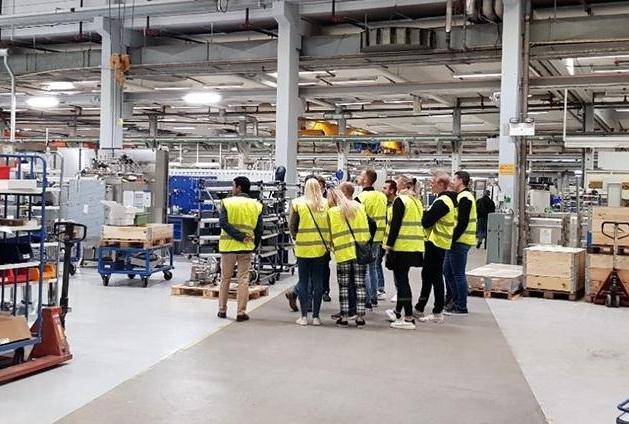 Grupp människor i gula västar i en industri. Foto.
