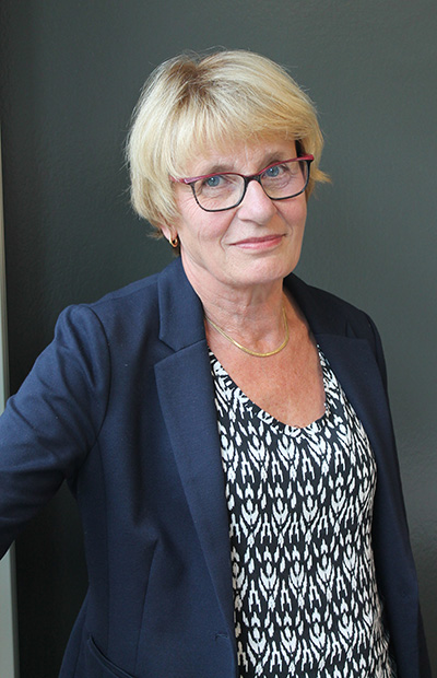 Kvinna, kort blont hår, mörka glasögon, blå kavaj.