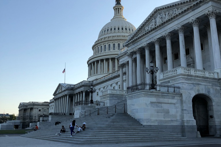 Kongressbyggnaden i Washington, flagga på halv stång framför. Blå ton som i skymningen