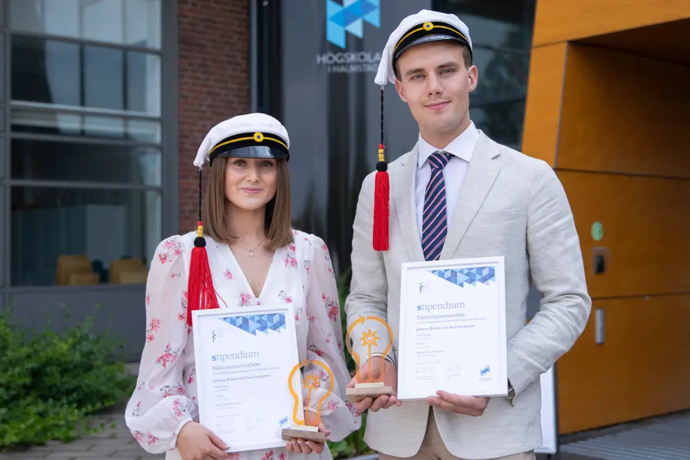 Två finklädda studenter ler mot kameran. Båda håller i ett varsitt diplom och statyett. Foto.