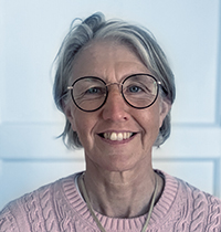 Man with grey hair and small glasses wearing grey suit smiling into the camera.