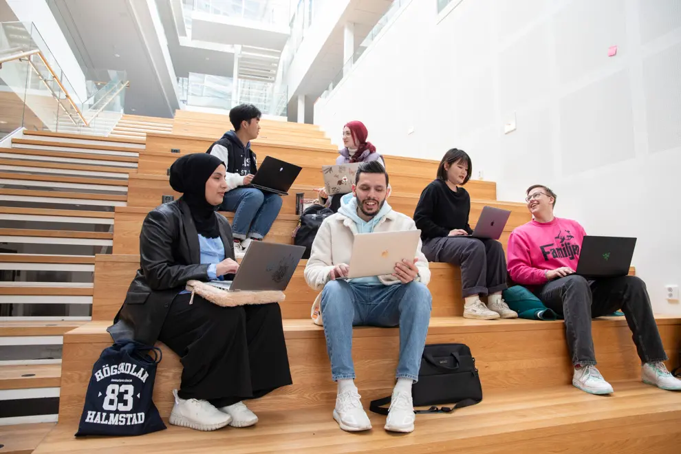 Sex glada studenter sitter i en trappa med sina bärbara datorer.
