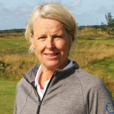 Blond kvinna i kort hår står på en golfbana och ler mot kameran. Foto.