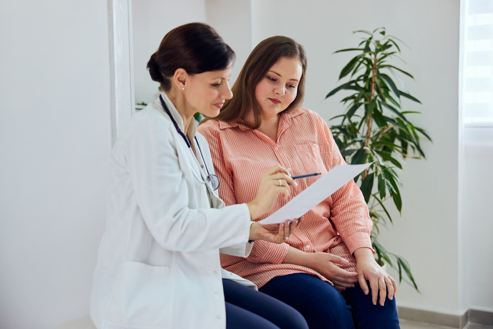 A doctor talks with her patient with a piece of paper in front of them.