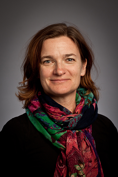 Portrait of a smiling dark-haired woman wearing a black top, a brightly coloured scarf around her neck. Photo.