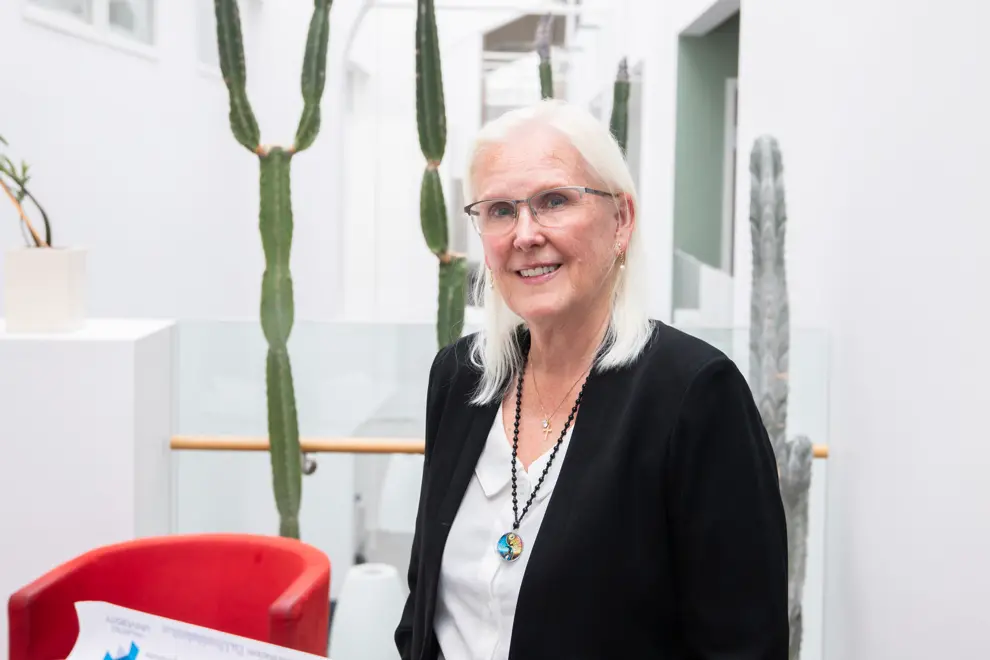 En person med långt ljust hår och glasögon ler in i kameran. Foto
