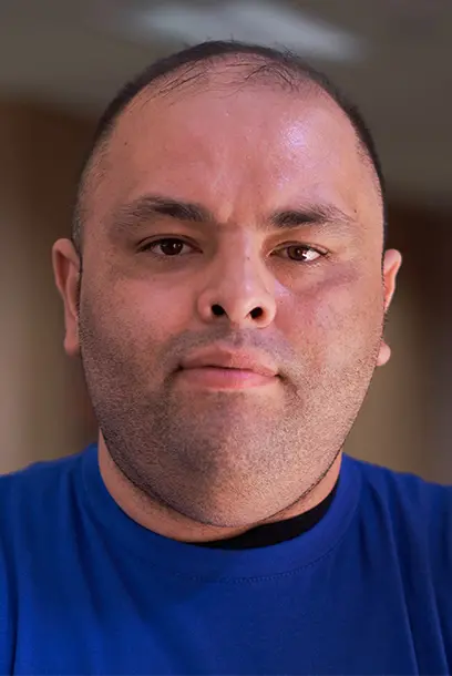 A man in a blue t-shirt looks in the camera.