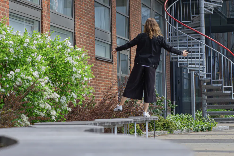 En kvinna balanserar på ett ben på en parkbänk. Foto