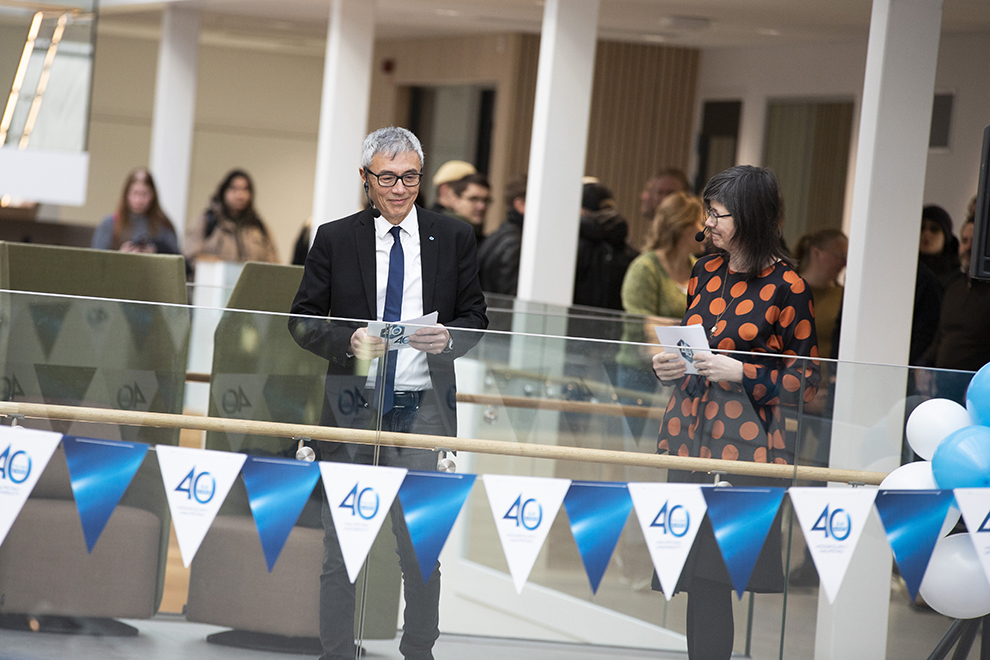Flags are hanging over an open space with people on different floors. Photo.