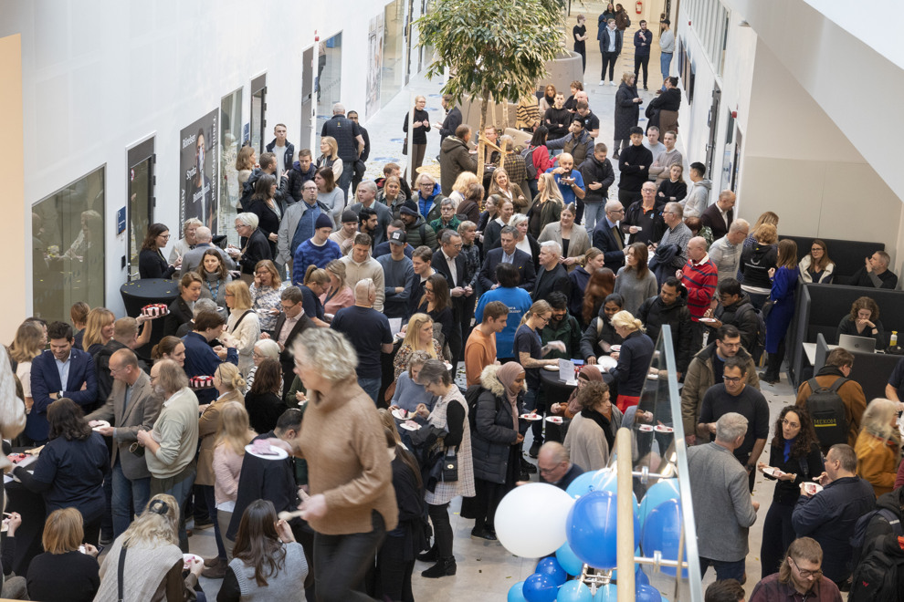 People mingling in a an open space eating cake. Photo.