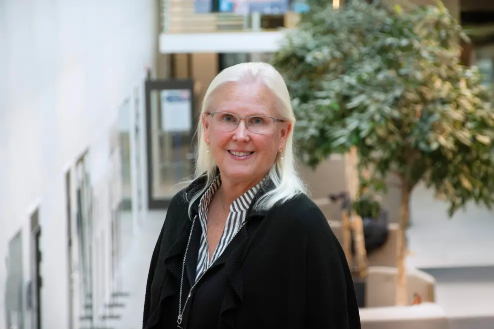 En person med långt ljust hår och glasögon ler in i kameran. Foto