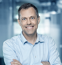 Man with grey hair and small glasses wearing grey suit smiling into the camera.