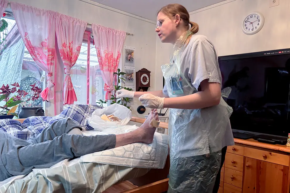 En sjuksköterska lägger om ett sår på en person som ligger i en säng.