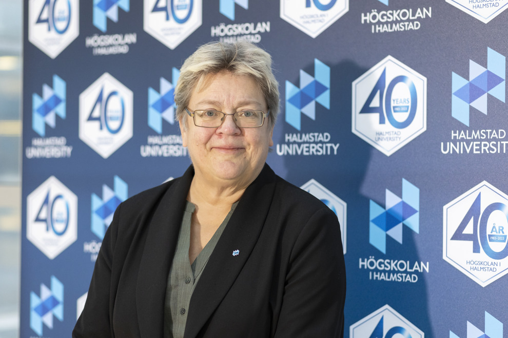 Woman in short hair and glasses is standing in front of a wall of anniversary symbols.