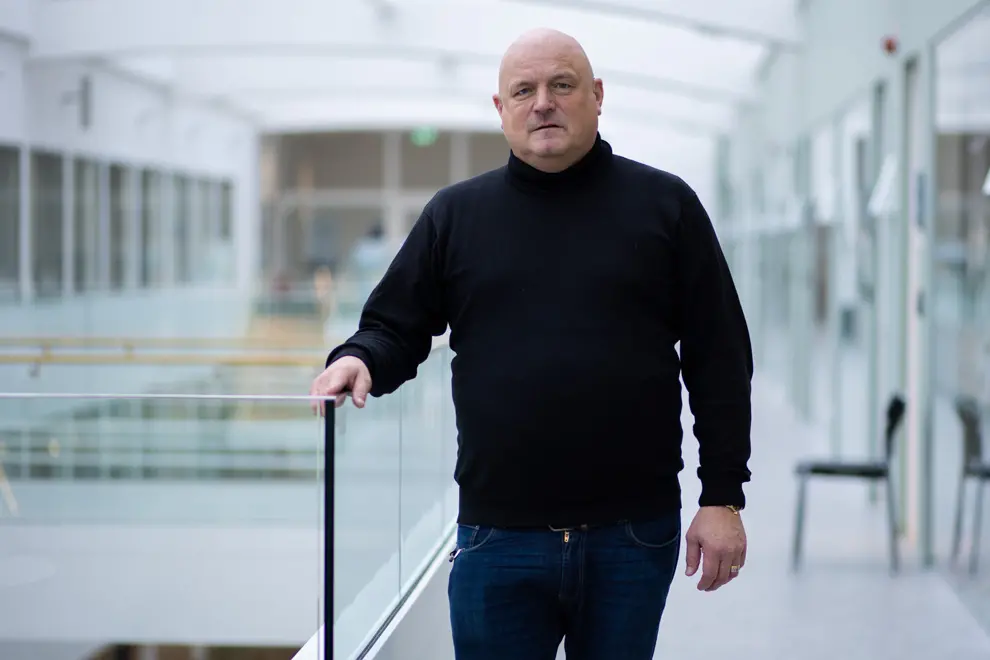 En man i svart tröja står på en balkong i inomhusmiljö.