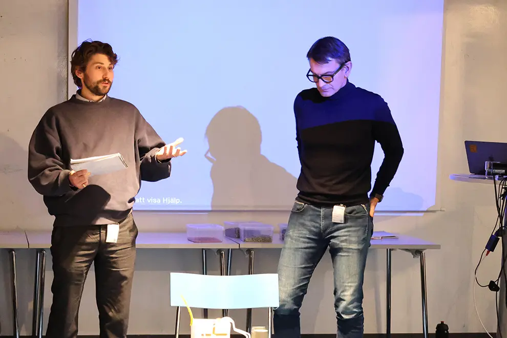 Två män står och presenterar framför en projektor. Foto