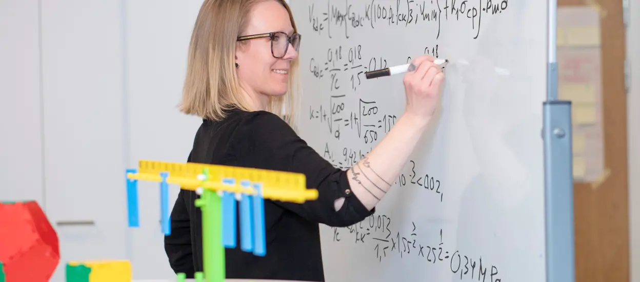 En kvinna skriver på en whiteboard med en tuschpenna. Foto.