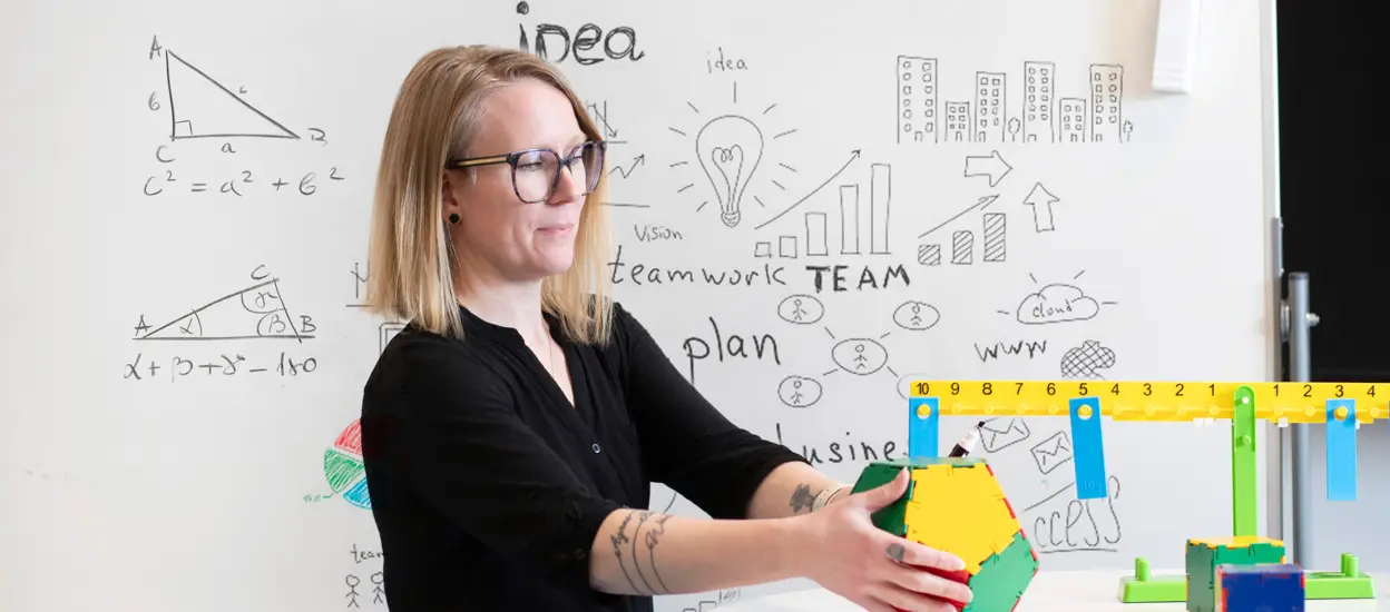 En kvinna står framför en whiteboard och sträcker sig efter en boll. Foto.