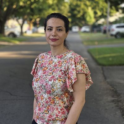 Porträtt av en kvinna som står på en väg omgiven av grönska. Foto.