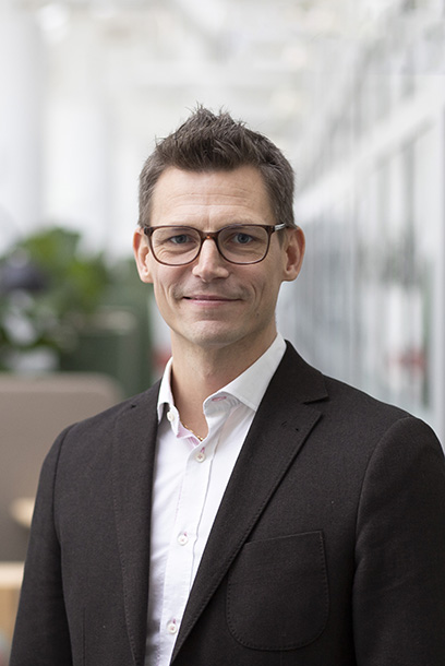 A man with glasses and a black jacket looks into the camera. Photo.