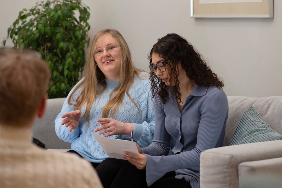 Två personer sitter i en soffa och samtalar. Foto.