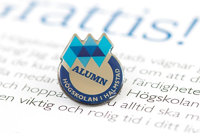 Bilden visar en in-zoomad pin med texten texten Alumn Högskolan i Halmstad och Högskolan i Halmstads logotyp. Foto.