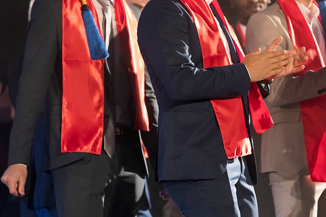 Several men in suits are standing in a line. Around their necks they have red shawls. Photo.